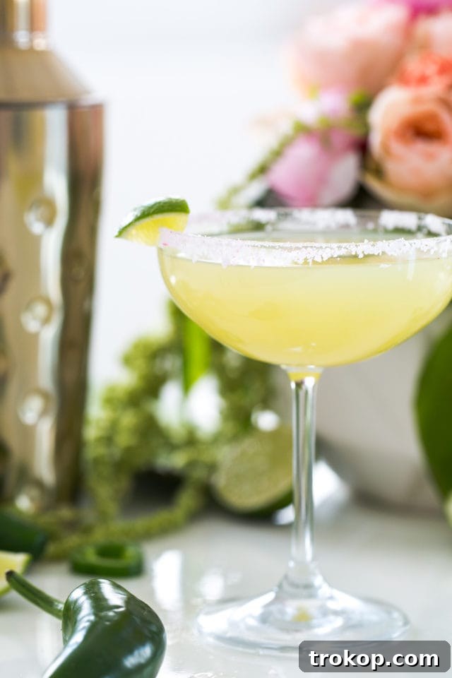 A hand holding a garnished jalapeño margarita with salt and lime