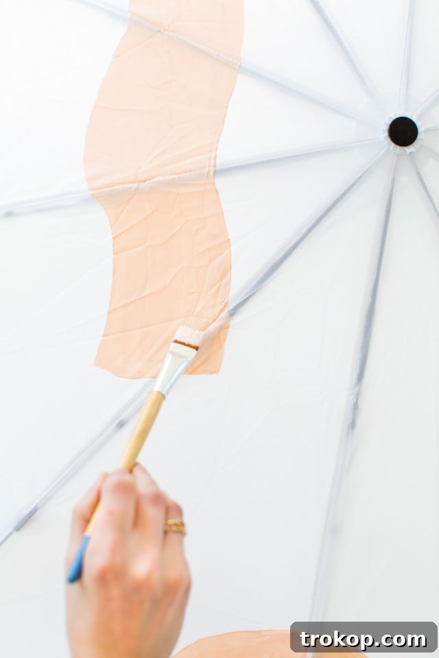 Artist's hand applying fabric paint to an umbrella panel, creating abstract shapes
