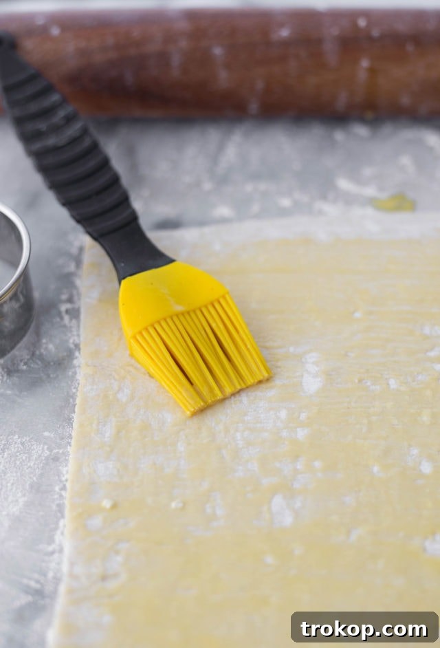 Puff pastry dough being rolled out and brushed with egg wash before cutting.