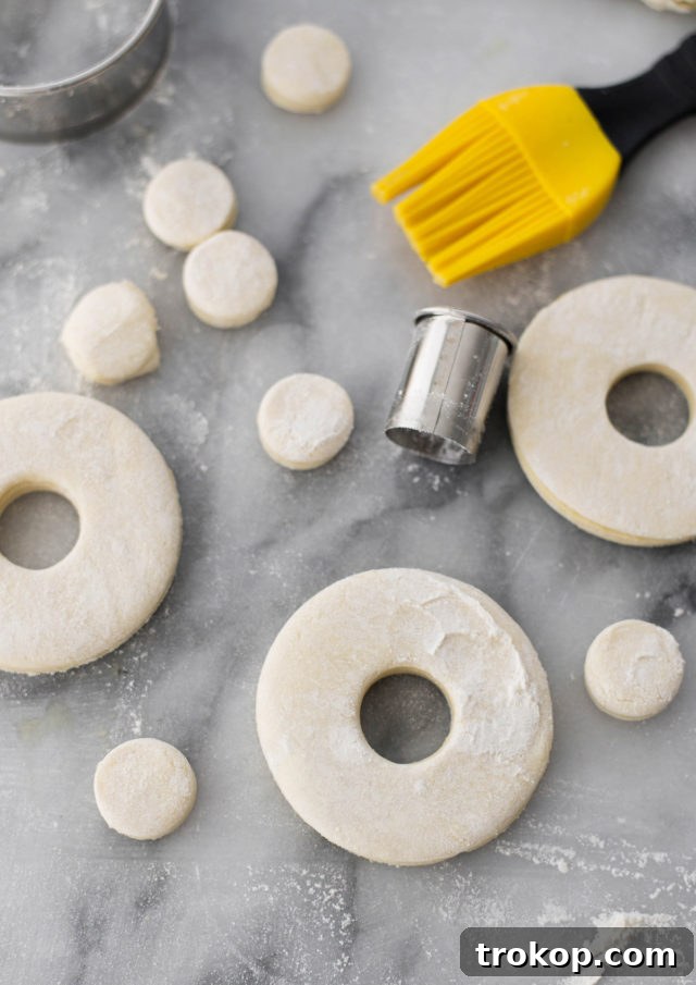 Donut shapes being cut from puff pastry dough using a biscuit cutter.