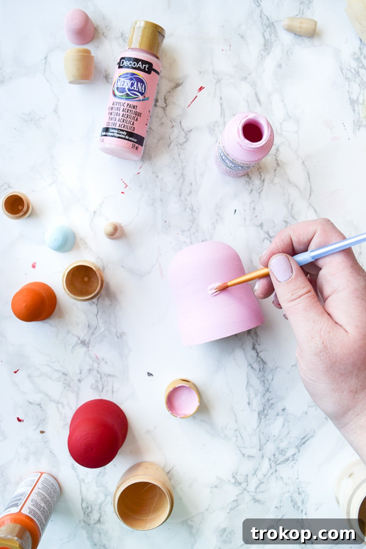 Detailed shot of a wooden nesting doll lid being carefully painted with a vibrant shade of acrylic craft paint, showcasing the two-coat application process for even coverage.