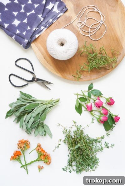 An overhead photo of fresh herbs and flowers arranged for a sage bundle, showing the starting materials for crafting.