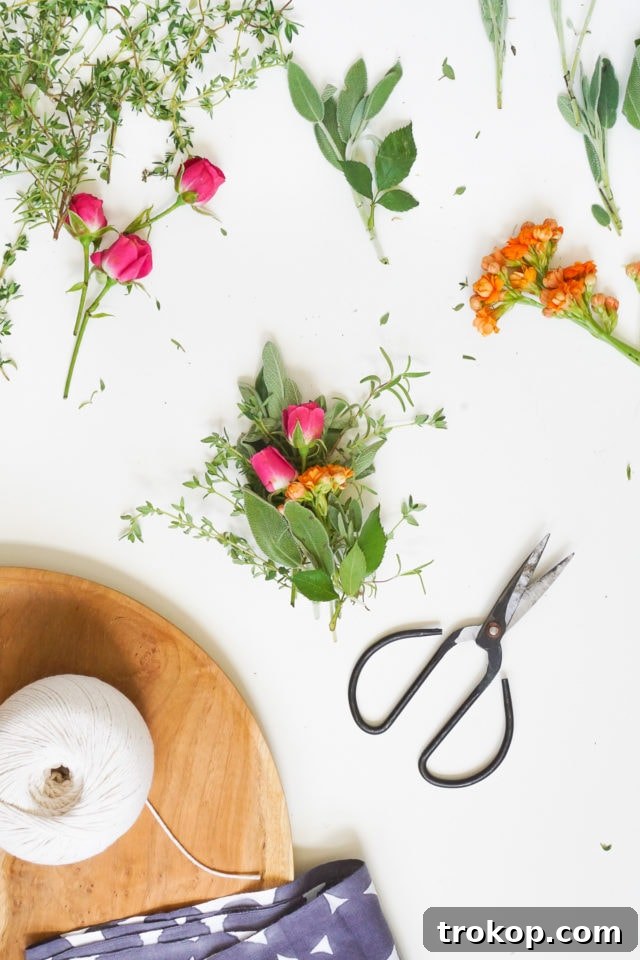 Freshly cut herbs and flowers laid out, ready for assembly into a sage bundle. The vibrant green sage leaves provide a base for delicate petals and other aromatic herbs.
