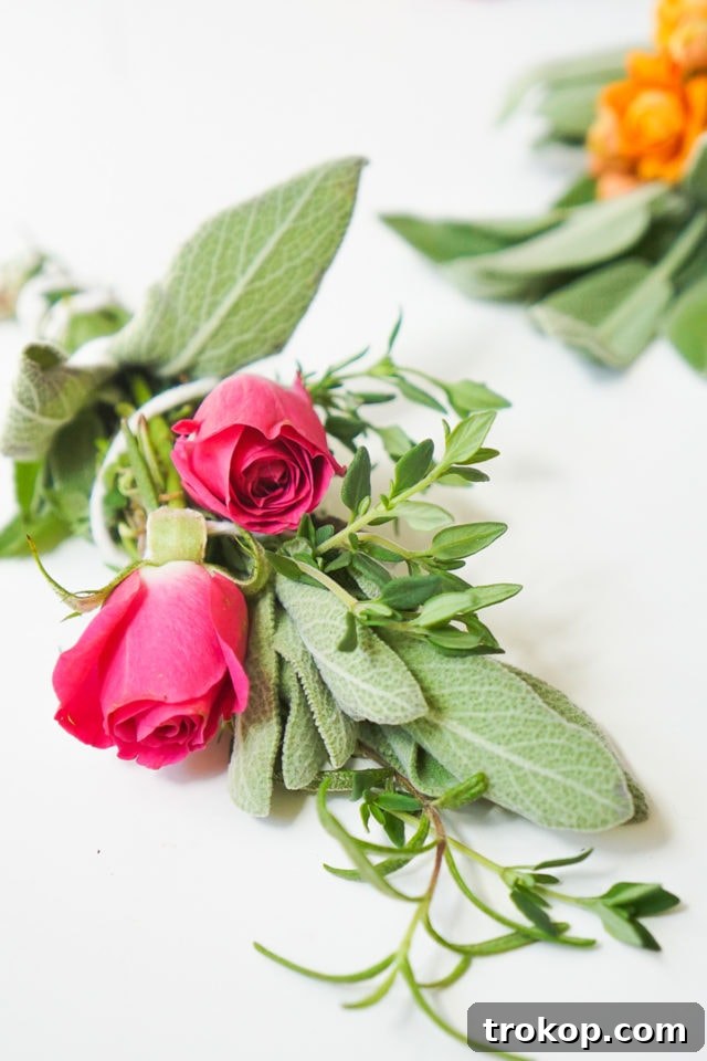 Three handmade sage bundles with flowers hanging upside down on a wooden dowel for drying, showcasing the completed DIY project in its curing phase.
