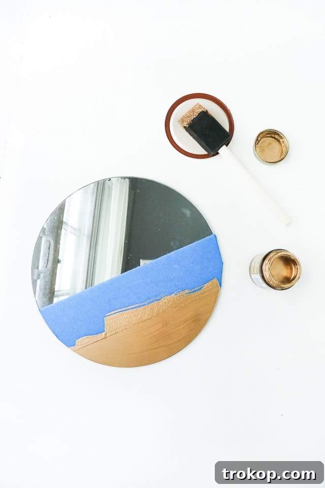 Step 1: Applying painter's tape and metallic gold paint to the bottom edge of the round mirror.