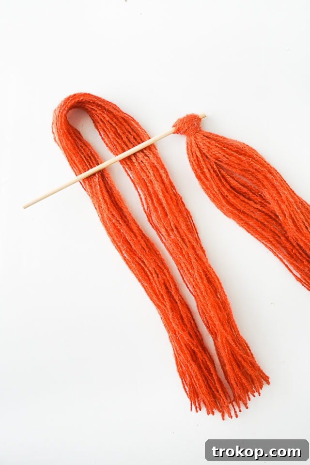 Step 3: Demonstrating how to tie a lark's head knot with a yarn bundle onto the wooden skewer.