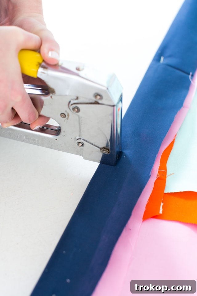 Staple gun securing layers of abstract fabric to a wooden dowel rod for a DIY wall art project