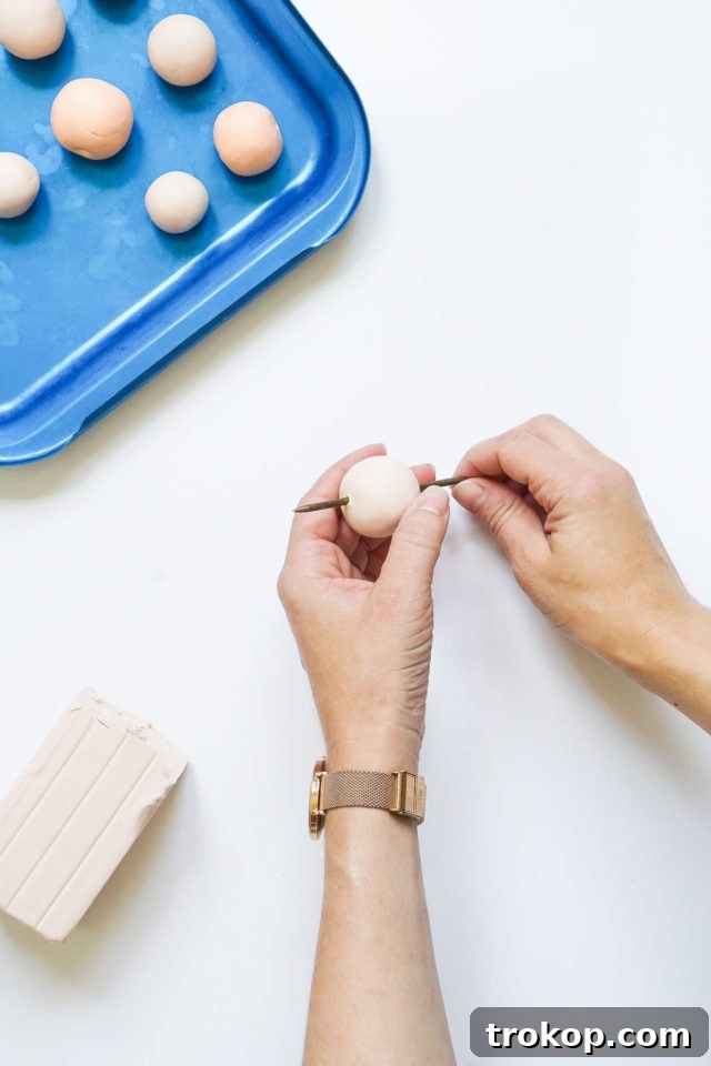 Hands rolling polymer clay into balls and poking holes with a tapestry needle, preparing beads for the blanket holder.