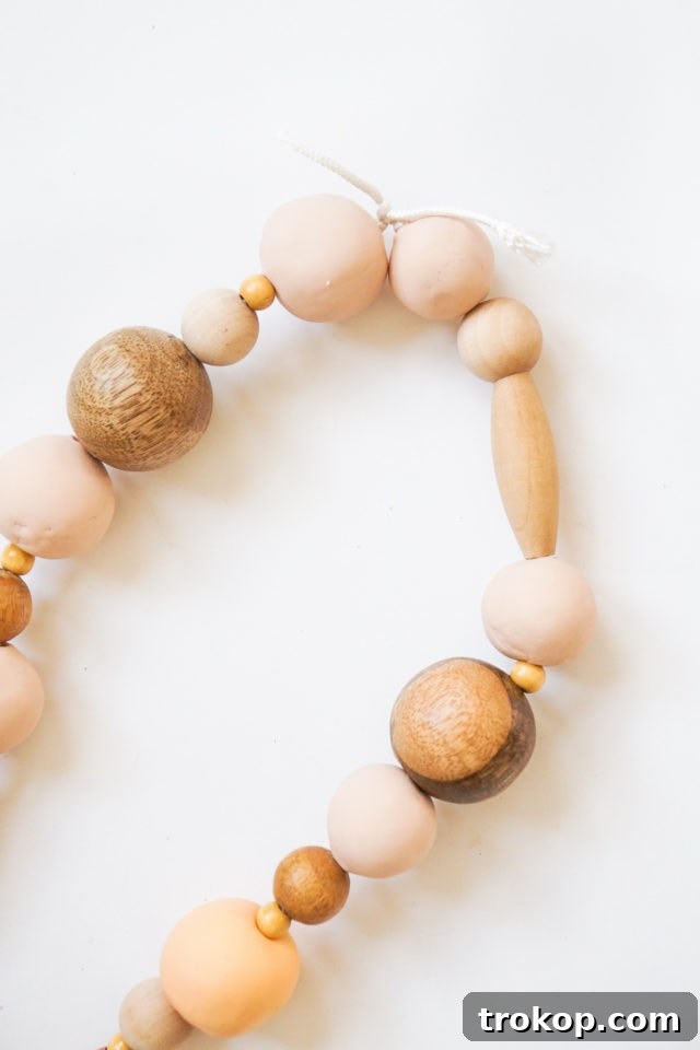 Someone stringing a mix of polymer clay and wood beads onto a long cord using a tapestry needle.