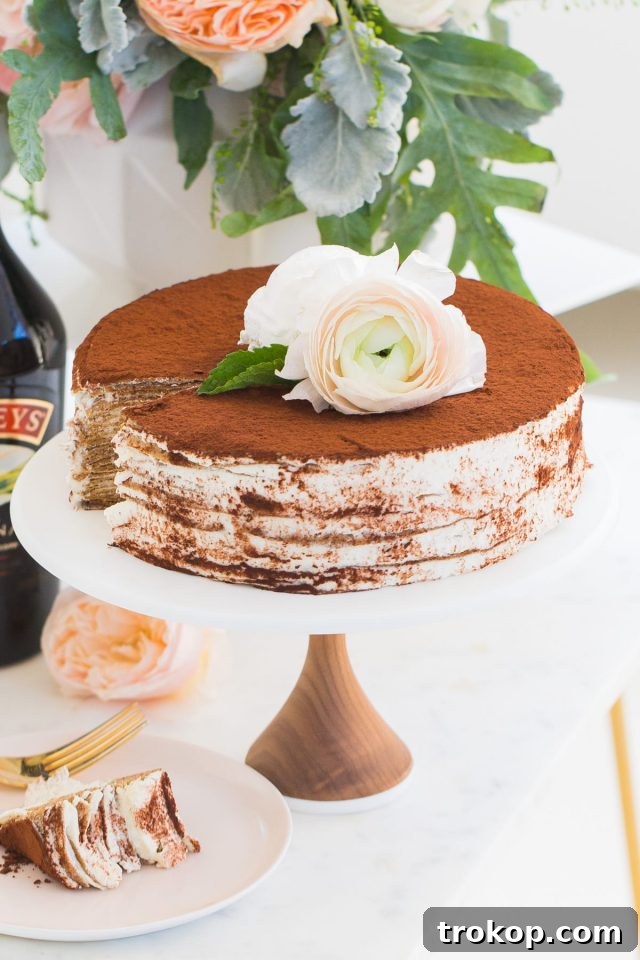 A slice of Baileys Tiramisu Crepe Cake on a white stand, showcasing delicate layers of crepes and creamy filling.