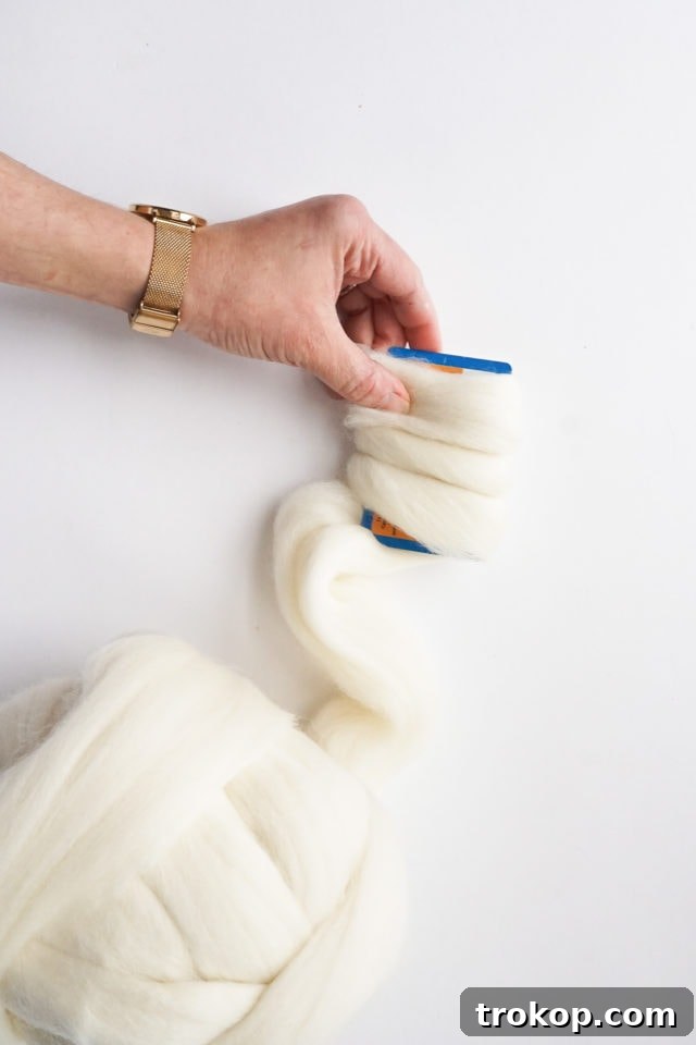 Wrapping wool roving around a plastic card to create pom-poms.