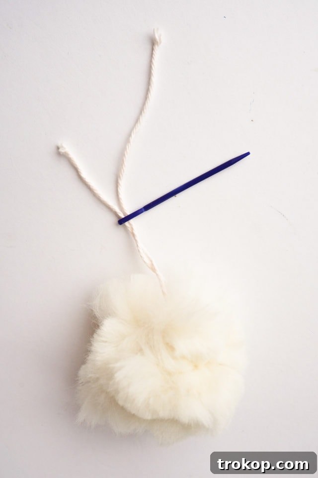 Threading the yarn tails of a pom-pom through a tapestry needle.