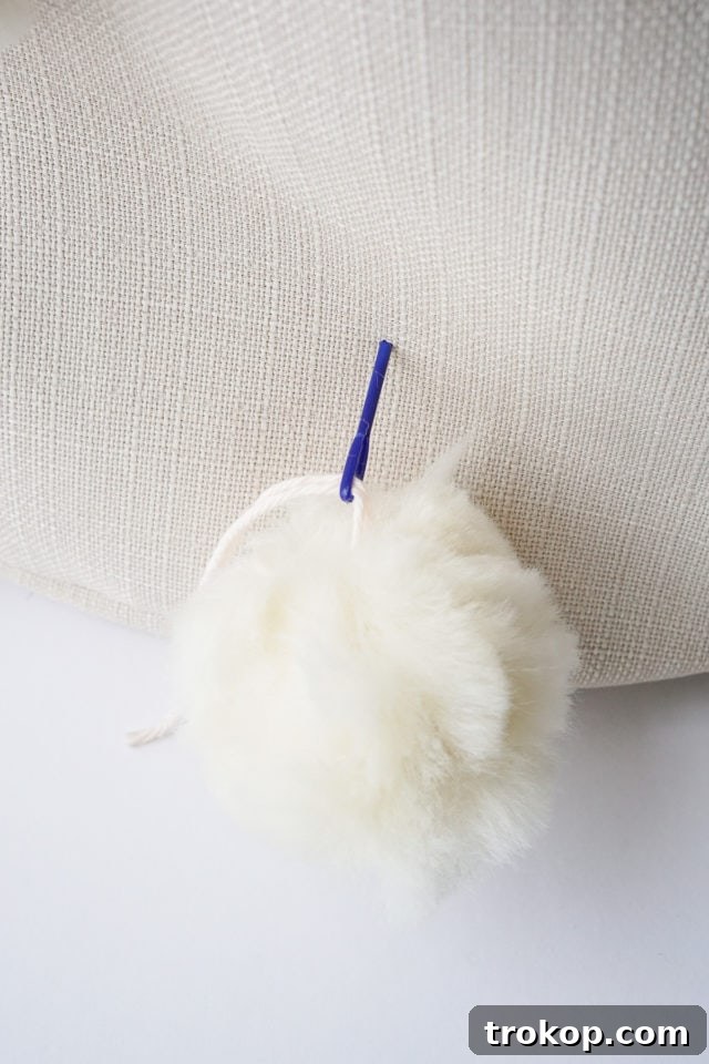 Attaching a pom-pom to the fabric bin by threading yarn through.