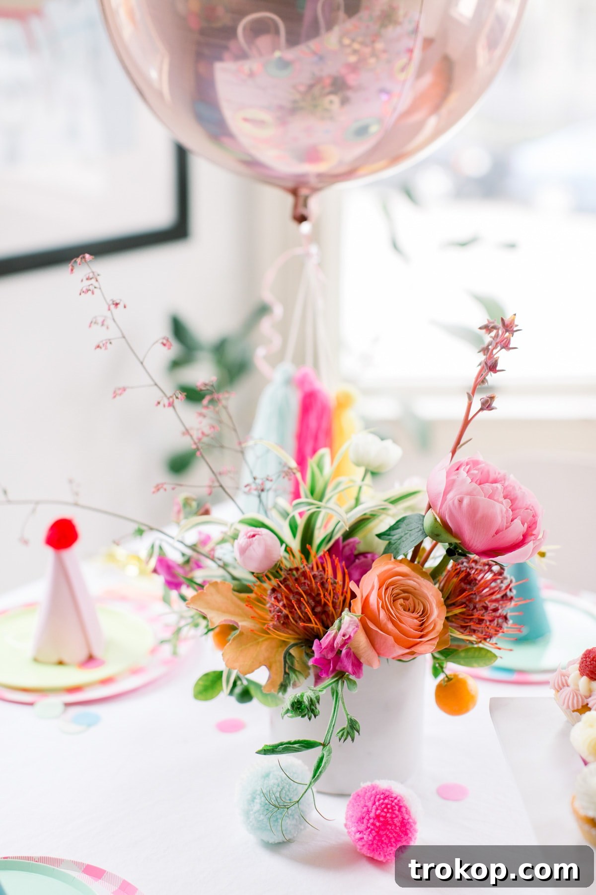 Guests enjoying the festive atmosphere, seated on white bistro chairs amidst the vibrant decorations and playful pom pom accents.
