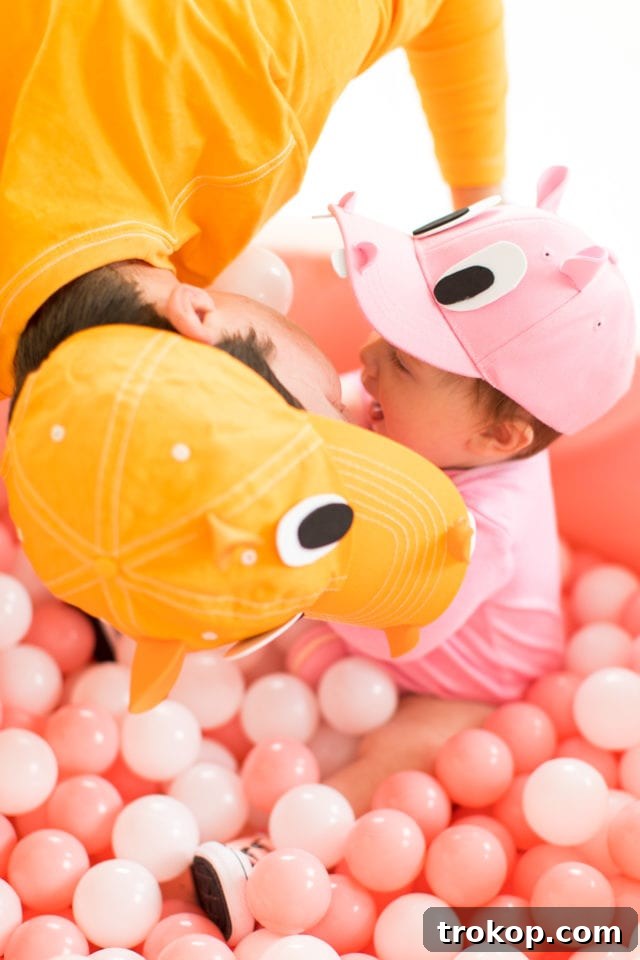 A heartwarming close-up of a family member in a DIY Hungry Hungry Hippos costume planting a 'hippo kiss' on the adorable baby, who is also dressed as a hippo. This candid moment captures the loving spirit and fun of this unique family Halloween costume idea.