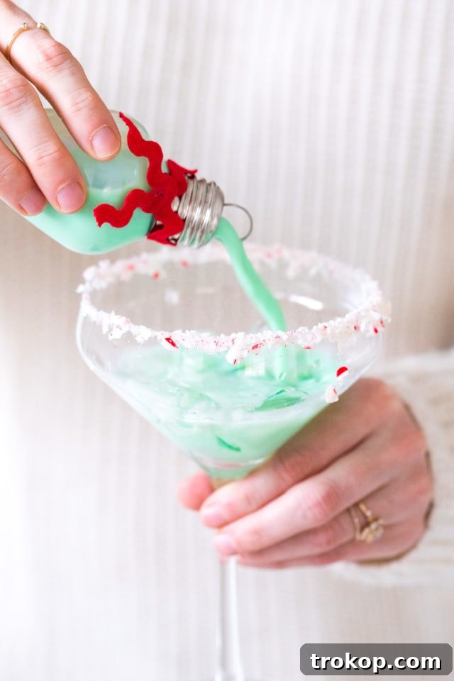 Homemade Holiday Cocktail Baubles 3 Hands pouring a mint green rumchata cocktail into a clear ornament bulb.