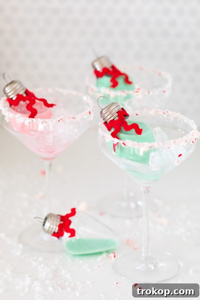 Homemade Holiday Cocktail Baubles 5 Close-up of a hand holding a clear Christmas cocktail ornament with a festive ribbon.