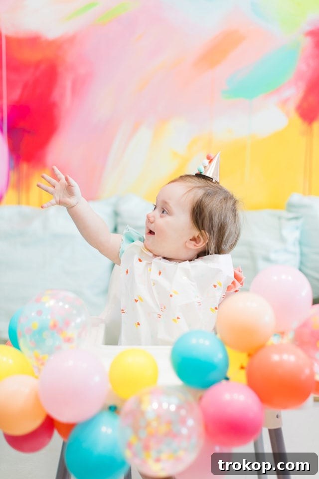 Gwen happily seated in her high chair adorned with a festive balloon garland by Sugar & Cloth