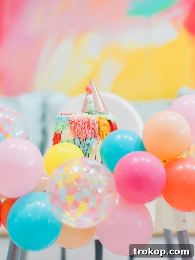 Rainbow smash cake alongside a colorful balloon garland from Glamfetti Co, perfect for a first birthday