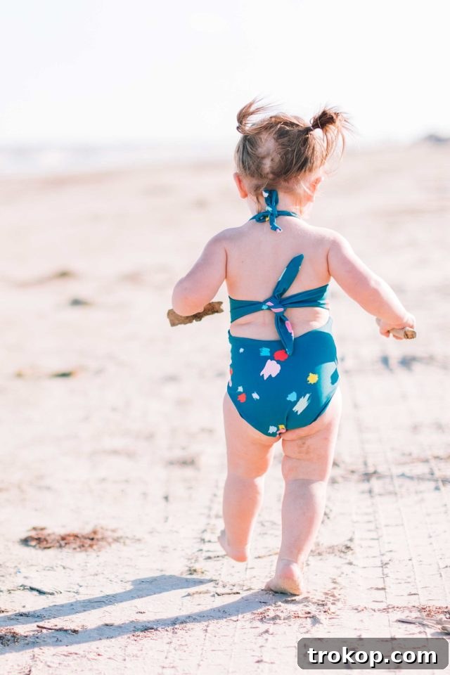 Gwen, Ashley Rose's daughter, smiling playfully in the confetti print Malibu one-piece swimsuit, featuring charming tie-back details from the Olivia + Ocean collection.