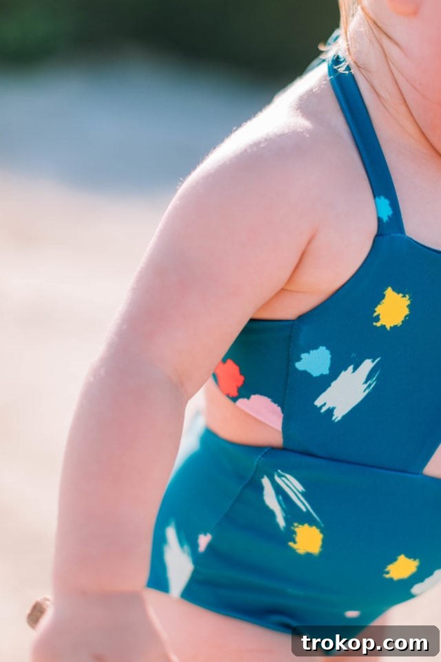 Gwen playing happily by the pool in her confetti print Malibu one-piece, demonstrating the comfort and sun-protective features of the Olivia + Ocean girls' swimwear.