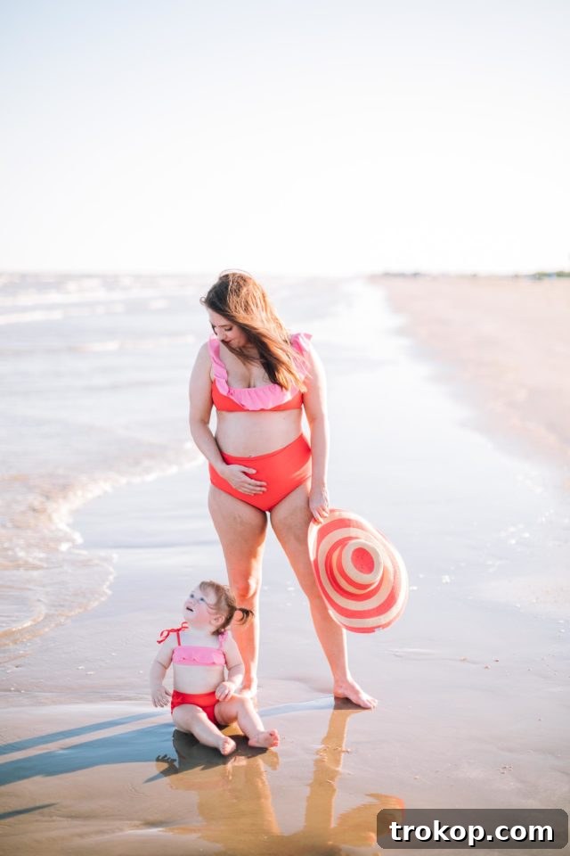 Ashley Rose of Sugar & Cloth in the coral red and perfect pink color block bikini, with her daughter Gwen in the matching high-waisted bikini, showcasing their coordinated and vibrant swimwear.