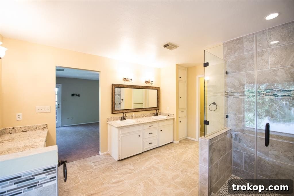 Before photo of an old double sink in a master bathroom, showcasing outdated faucets and a dull countertop, prior to a modern and stylish remodel by Sugar & Cloth.