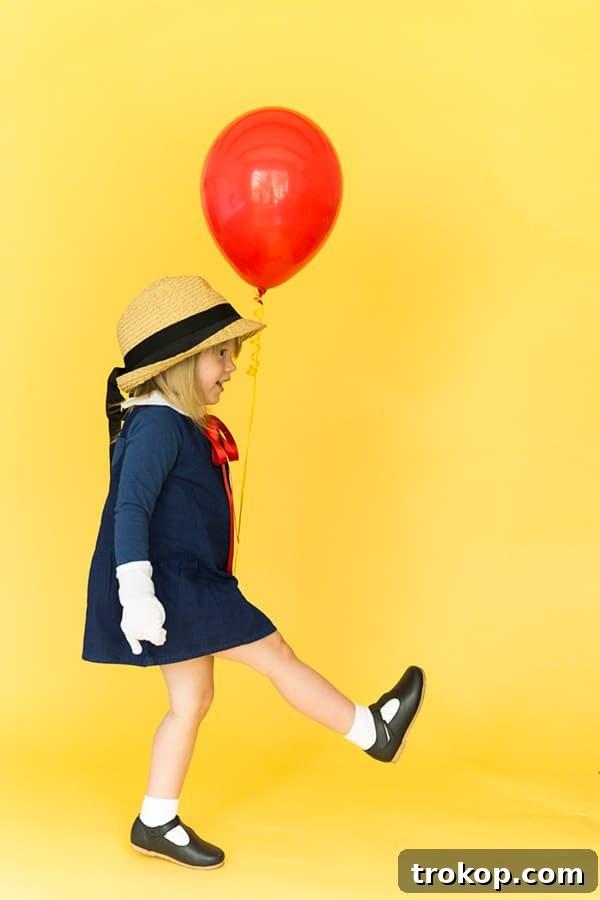 Girl dressed in a classic Madeline Halloween costume with a yellow hat and blue coat