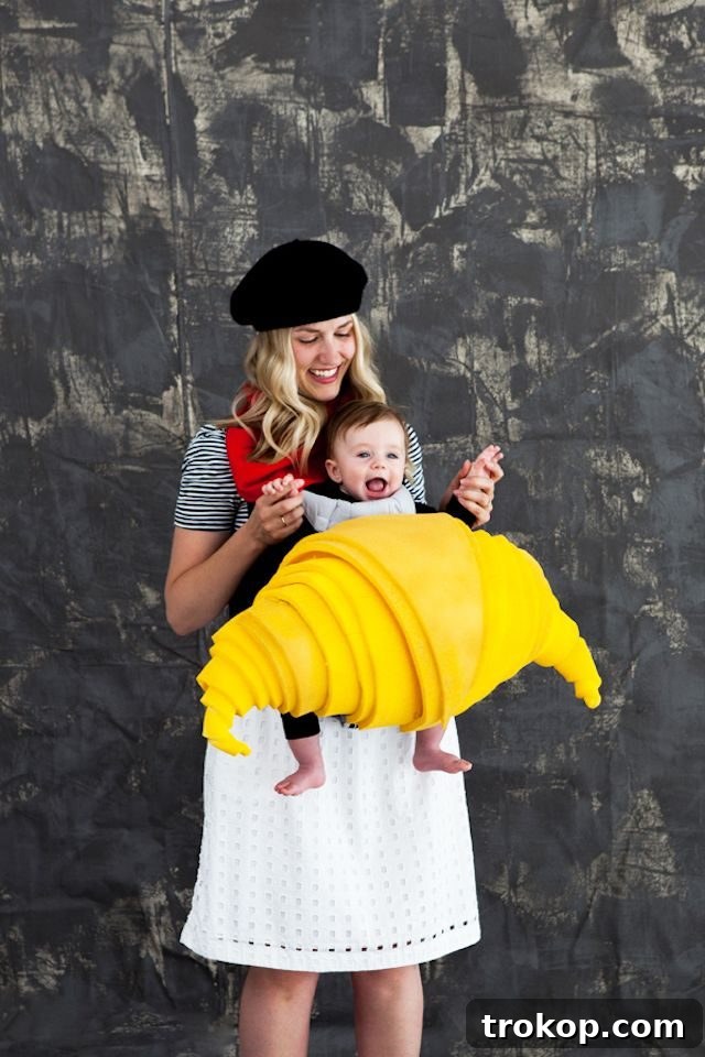 40 Spooktacular Family Halloween Costume Ideas 14 A mother dressed as a stylish French woman, holding her baby cosily dressed in a DIY croissant costume in a carrier.