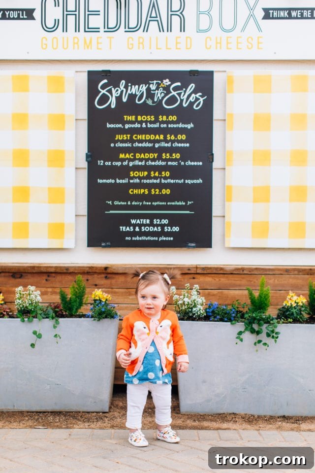 A child poses happily in front of the Cheddar Box food truck at the Silos, ready for a grilled cheese