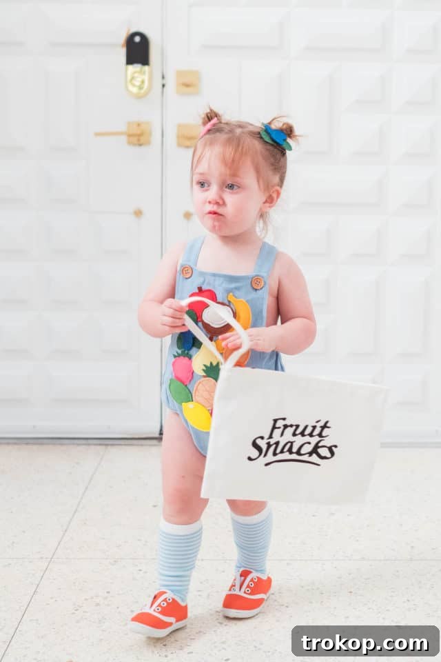 A charming photo of a toddler proudly wearing her DIY fruit snacks Halloween costume, complete with felt fruits.
