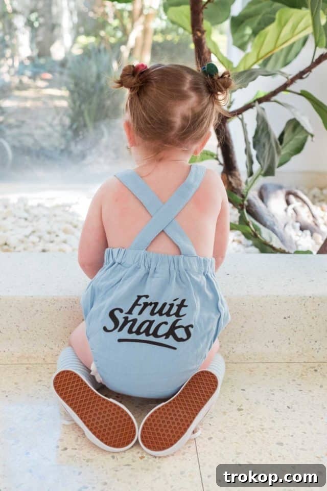 Close-up detail of a toddler's fruit snacks Halloween costume, featuring a romper with a brand logo and attached felt fruits.