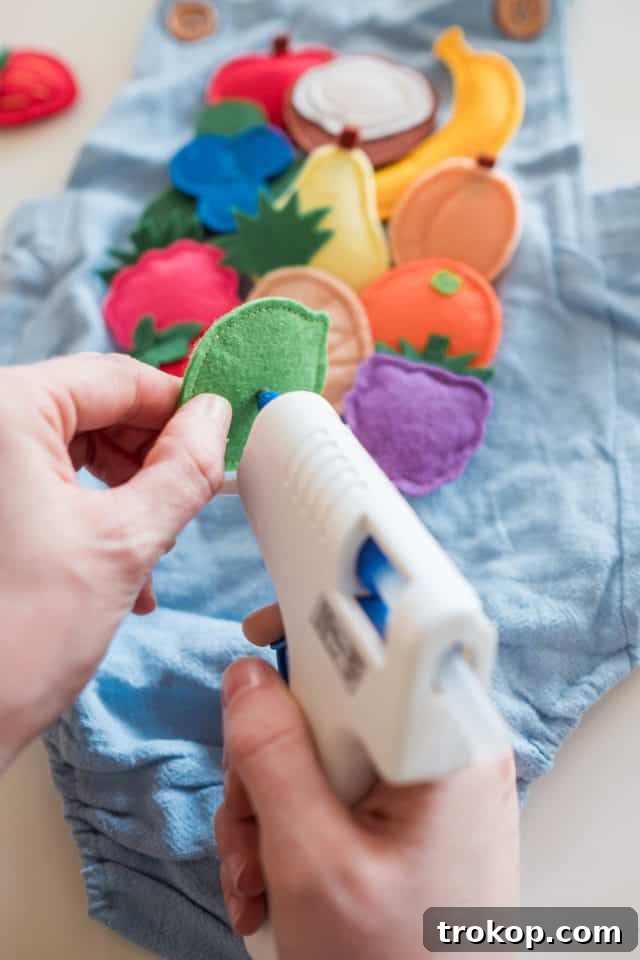 Felt fruit pieces being hot glued onto a blue baby romper, demonstrating the crafting process for the fruit snacks costume.