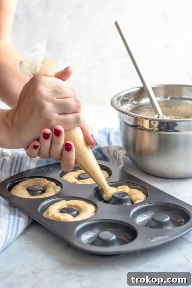 Gluten-free donut batter being expertly piped into donut pans, ensuring a clean and consistent shape, by top Houston lifestyle blogger Ashley Rose of Sugar & Cloth.