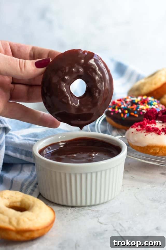 A baked gluten-free donut being dipped into luscious chocolate ganache, illustrating a perfect coating technique, by top Houston lifestyle blogger Ashley Rose of Sugar & Cloth.