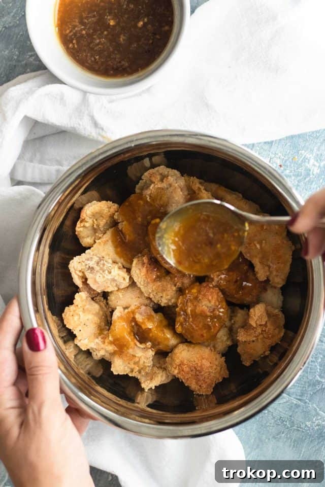 Zesty Orange Chicken 7 A hand mixing the chili sauce for easy orange chicken in a saucepan, highlighting the rich texture and vibrant color, by Houston lifestyle blogger Ashley Rose of Sugar & Cloth.