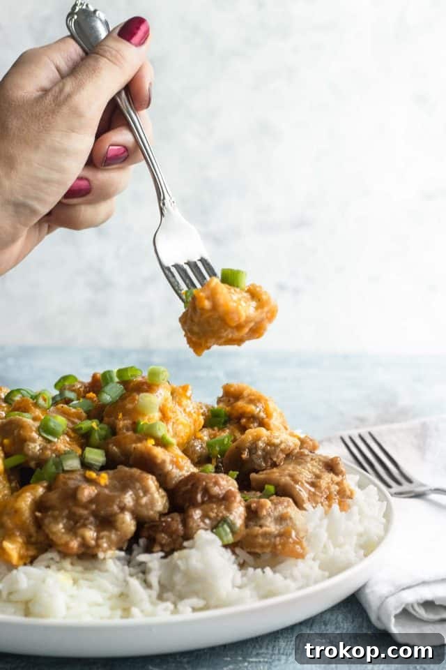 Zesty Orange Chicken 9 Person taking a bite of the easy orange chicken dinner, garnished with green onions, showcasing a delicious homemade meal by Houston lifestyle blogger Ashley Rose of Sugar & Cloth.