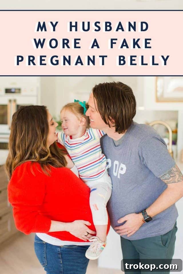 photo of a dad wearing a fake pregnant belly, looking down at his simulated bump