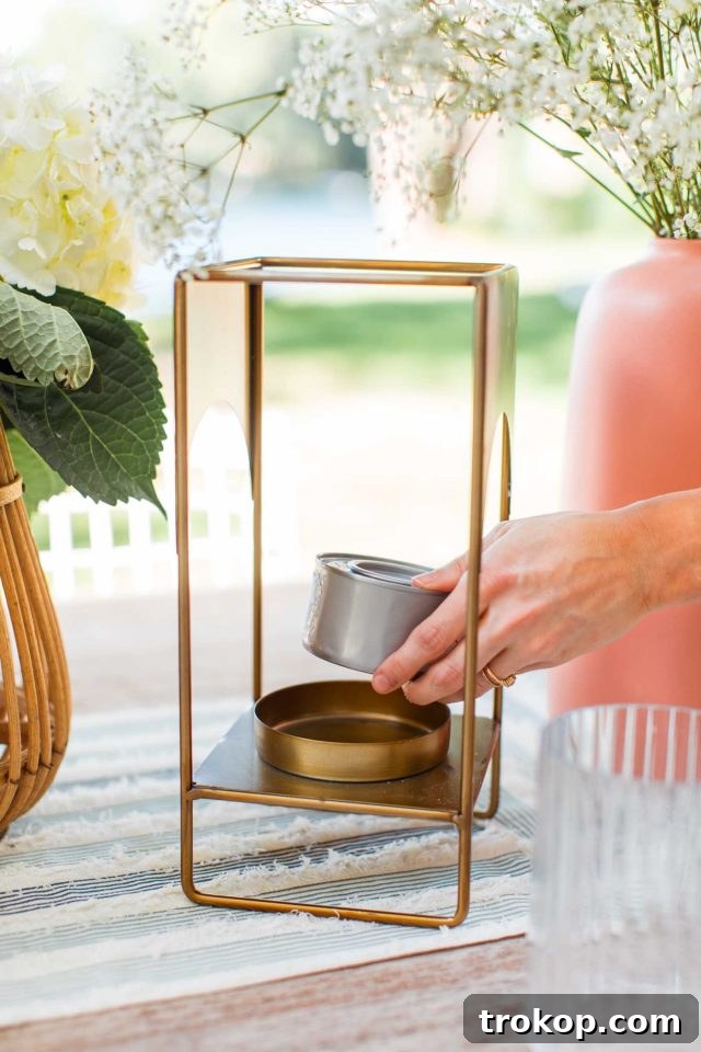 A hand placing a lit Sterno gel can inside a gold lantern, demonstrating a simple hack to keep flies away from outdoor dining.
