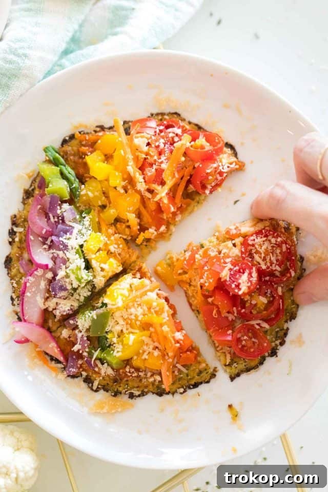 Guilt-Free Cauliflower Pizza Crust for Your Low-Carb Lifestyle 13 Overhead view of a hand reaching for a vibrant rainbow veggie-topped pizza with a cauliflower crust