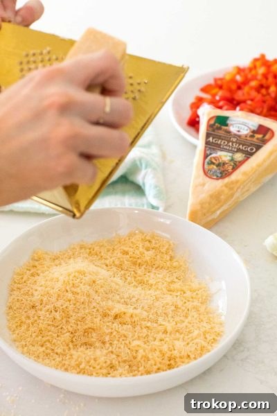 Freshly grated Stella Aged Asiago cheese wedge on a cutting board