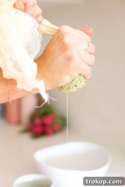 Hands wringing out excess water from steamed cauliflower in a cheesecloth