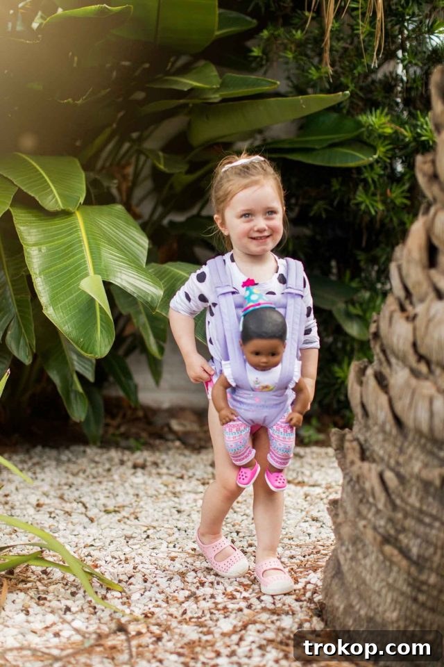 Toddler girl carrying her baby doll in a carrier, showcasing imaginative play and nurturing behavior