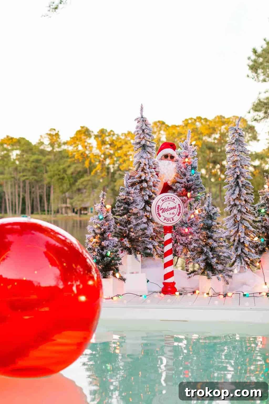 Santa's Poolside Paradise Christmas 6 Man in a Santa suit posing next to a festive outdoor fire pit and a lavishly decorated pool area for Christmas.