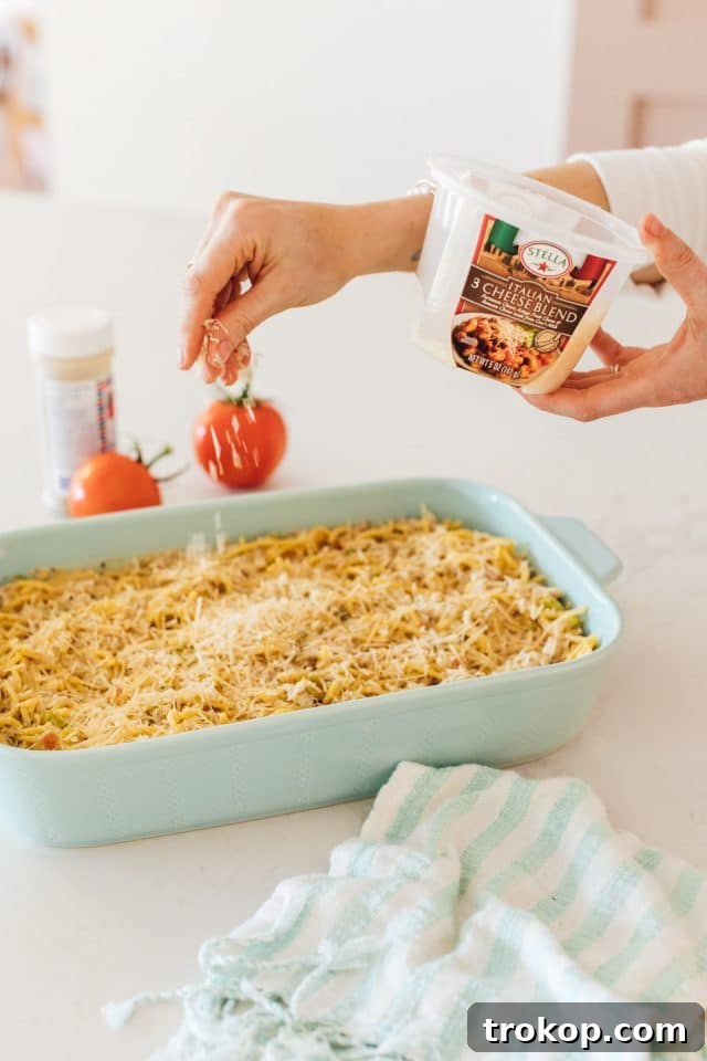 Photo of the chicken pasta bake being topped with grated cheese by top Houston lifestyle blogger Ashley Rose of Sugar & Cloth