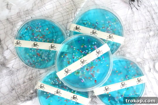DIY petri dish jell-o recipe A hand holding a Petri Dish Jello, decorated with skull ribbon, against a blurred background.