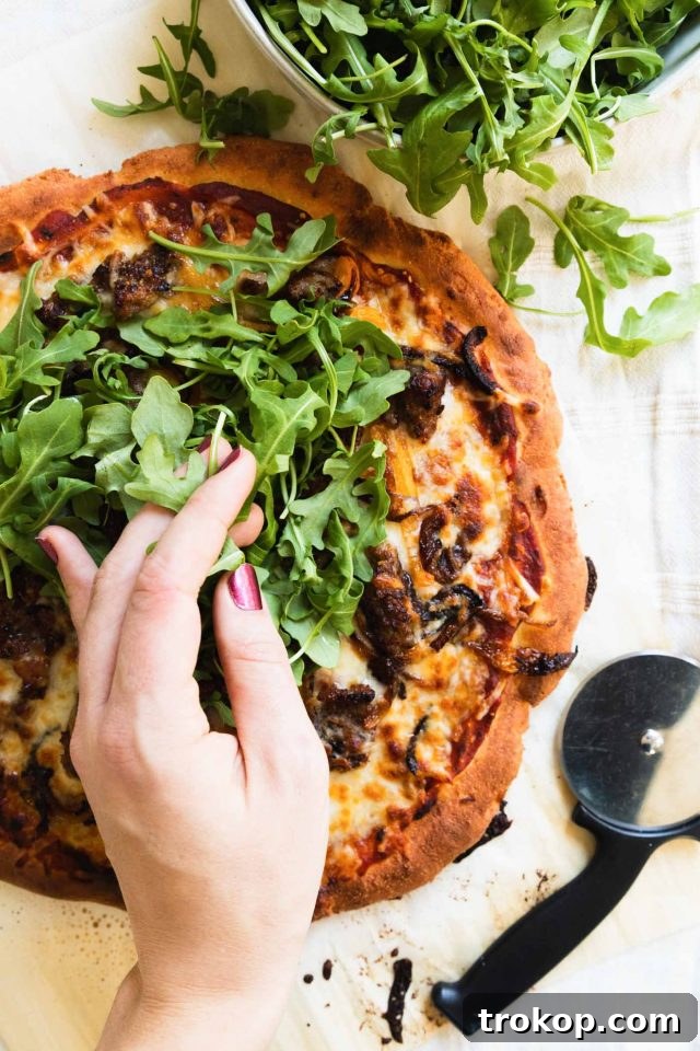 The Perfect Keto Pizza Crust 6 Fresh arugula being added as a topping to a hot keto pizza crust, highlighting healthy additions.