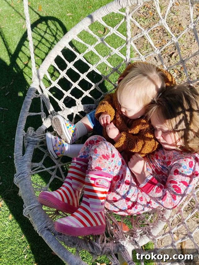 Two adorable little girls laughing together on a whimsical outdoor swing, enjoying the beautiful weather.