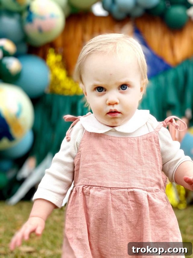 A young girl posing playfully in front of a charming baby shower backdrop, ready for celebration.