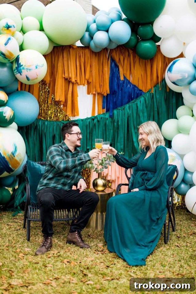 Your Essential Guide to a Drive-Thru Baby Shower 9 A mom and dad-to-be clinking champagne glasses in front of a festive drive-thru shower backdrop adorned with balloons